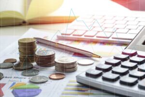 A couple reviews a household budget beside a laptop, savings envelope, calculator, and stack of bills.